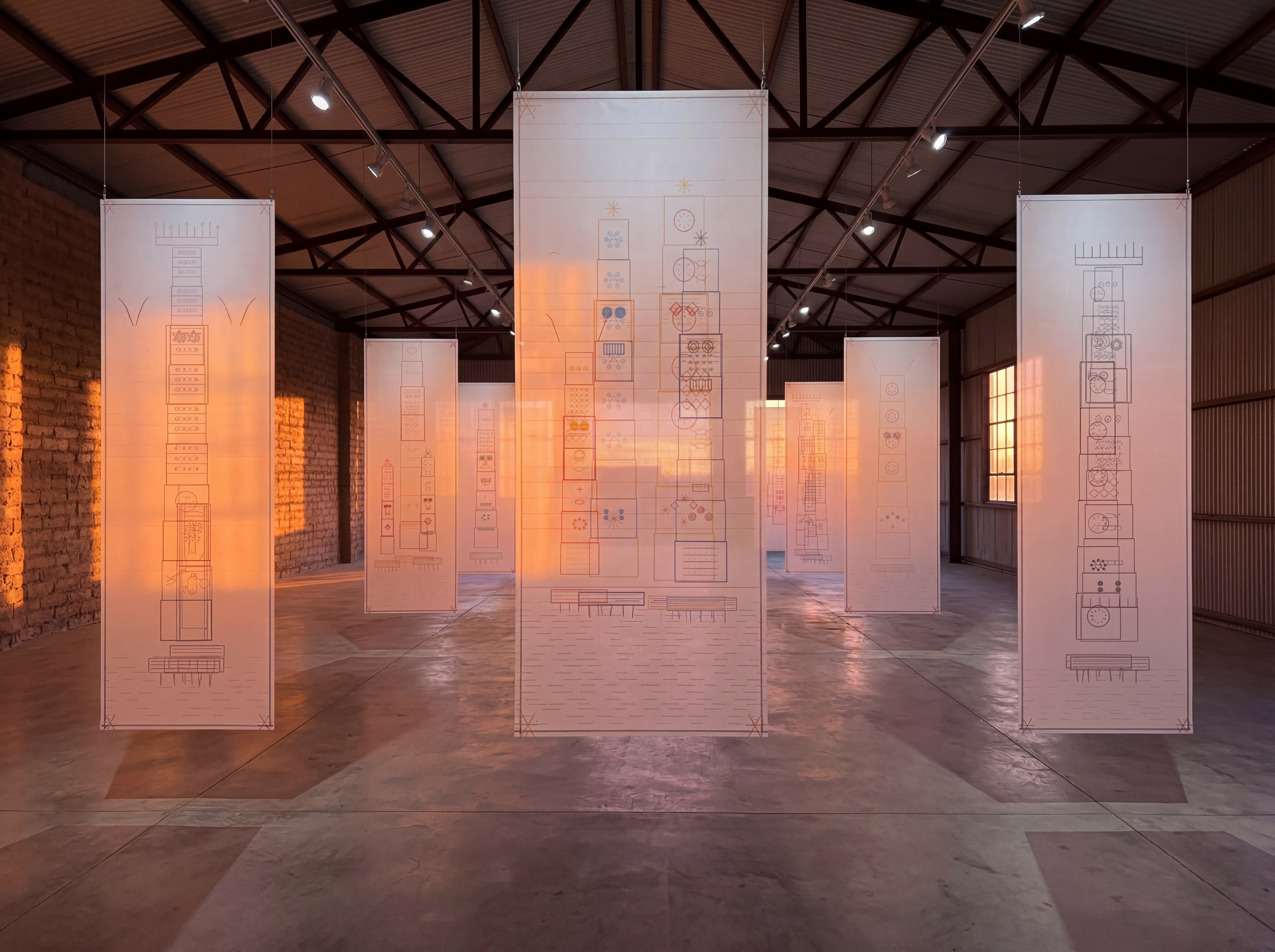 Golden-hour warehouse installation study — DATASPHERE 10 projected across a long gallery wall with suspended architectural paper panels in the foreground